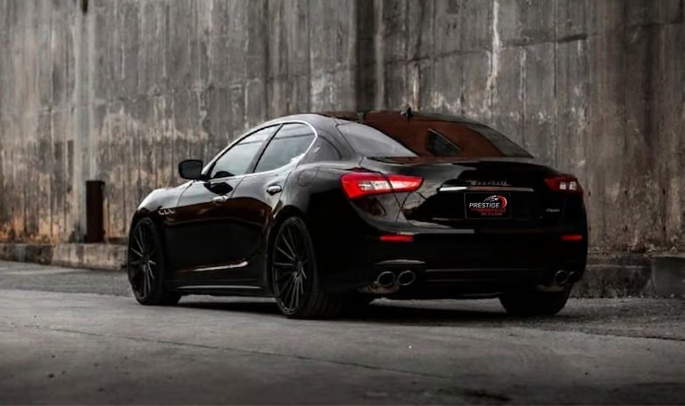 A detailed black Maserati Ghibli parked in front of a concrete wall, representative of the quality vehicles at Prestige Imports